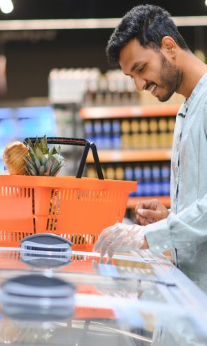 Portrait of happy Indian man standing in front of the product counter in a grocery store.